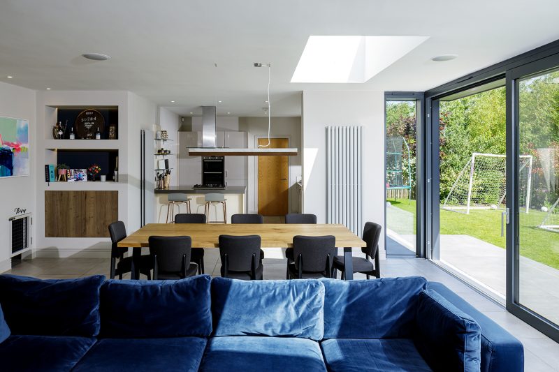 A modern living room with a dining table, blue sofa, and bifold doors.