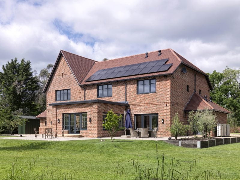 A large brick house surrounded by grass with an extension and solar panels on the roof.