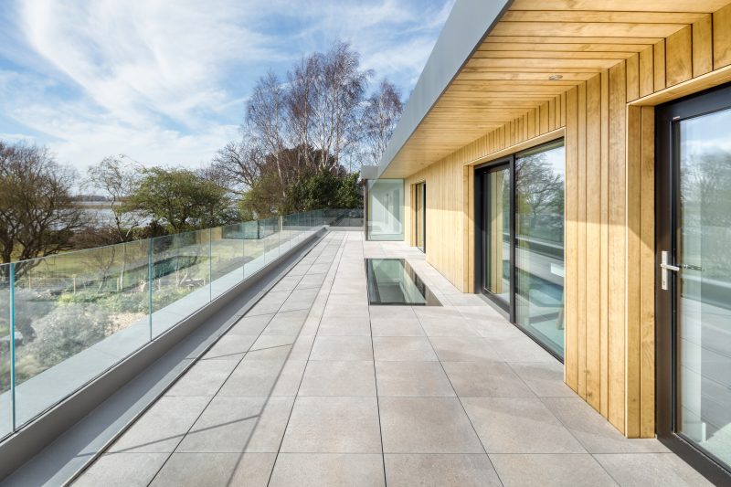 A long balcony on the edge of a house with a glass banister and a bespoke glass floor panel.