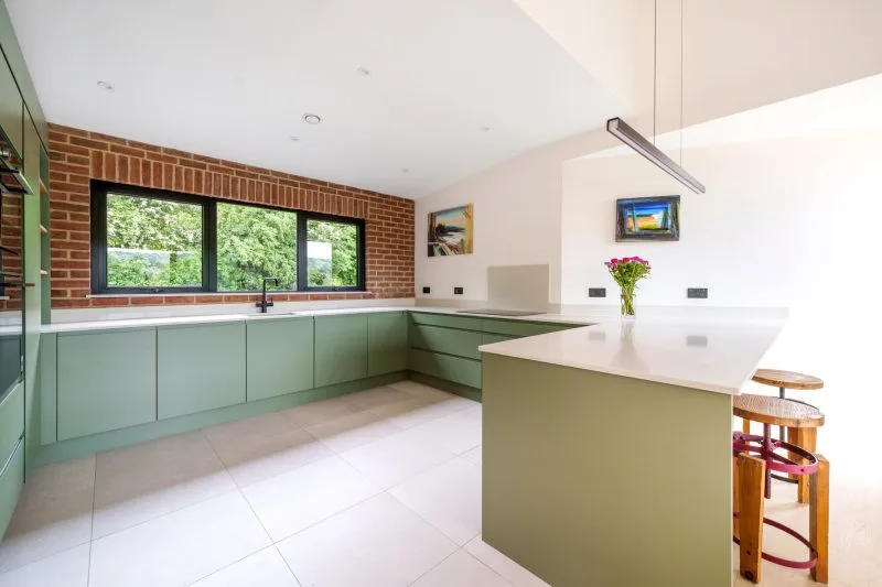 A large open-plan kitchen with a wrap-around kitchen and breakfast bar, with an exposed brick wall with aluminium windows installed.