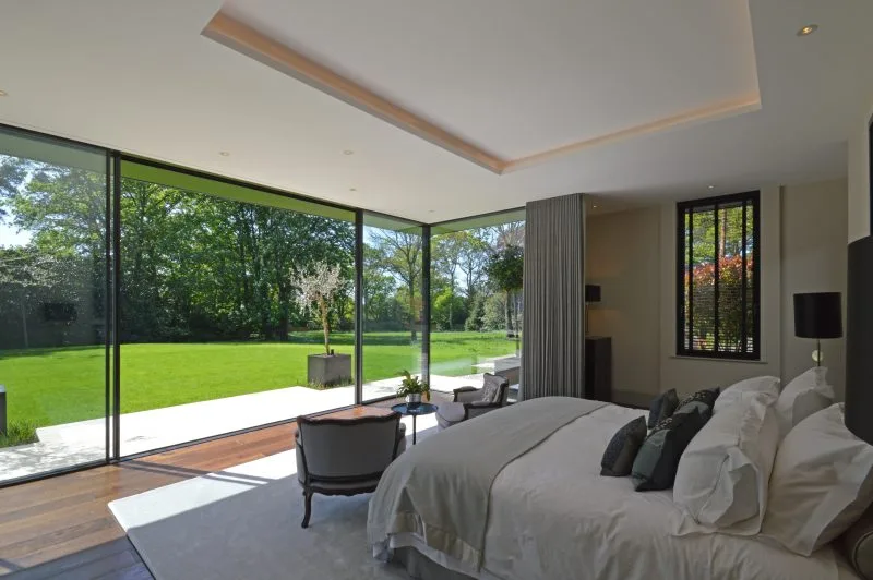 A bedroom with a wall of glass sliding doors that opens onto a patio and large garden.