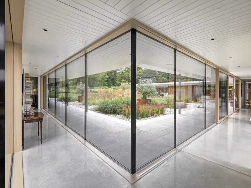 A modern hallway with floor-to-ceiling windows and sliding glass doors that lead onto a courtyard.